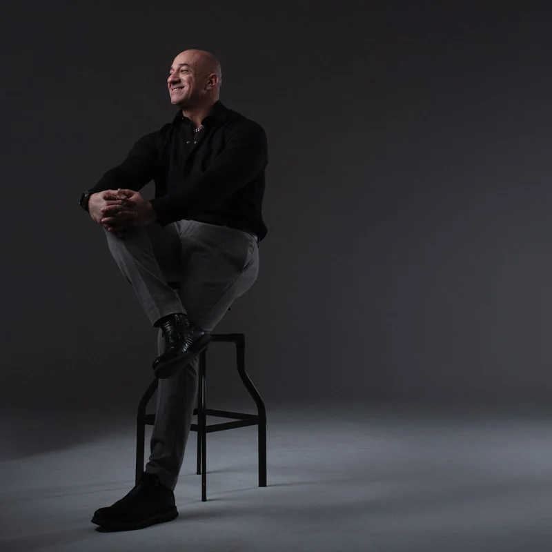 Akmal Kadri seated on a stool in a dark studio, smiling